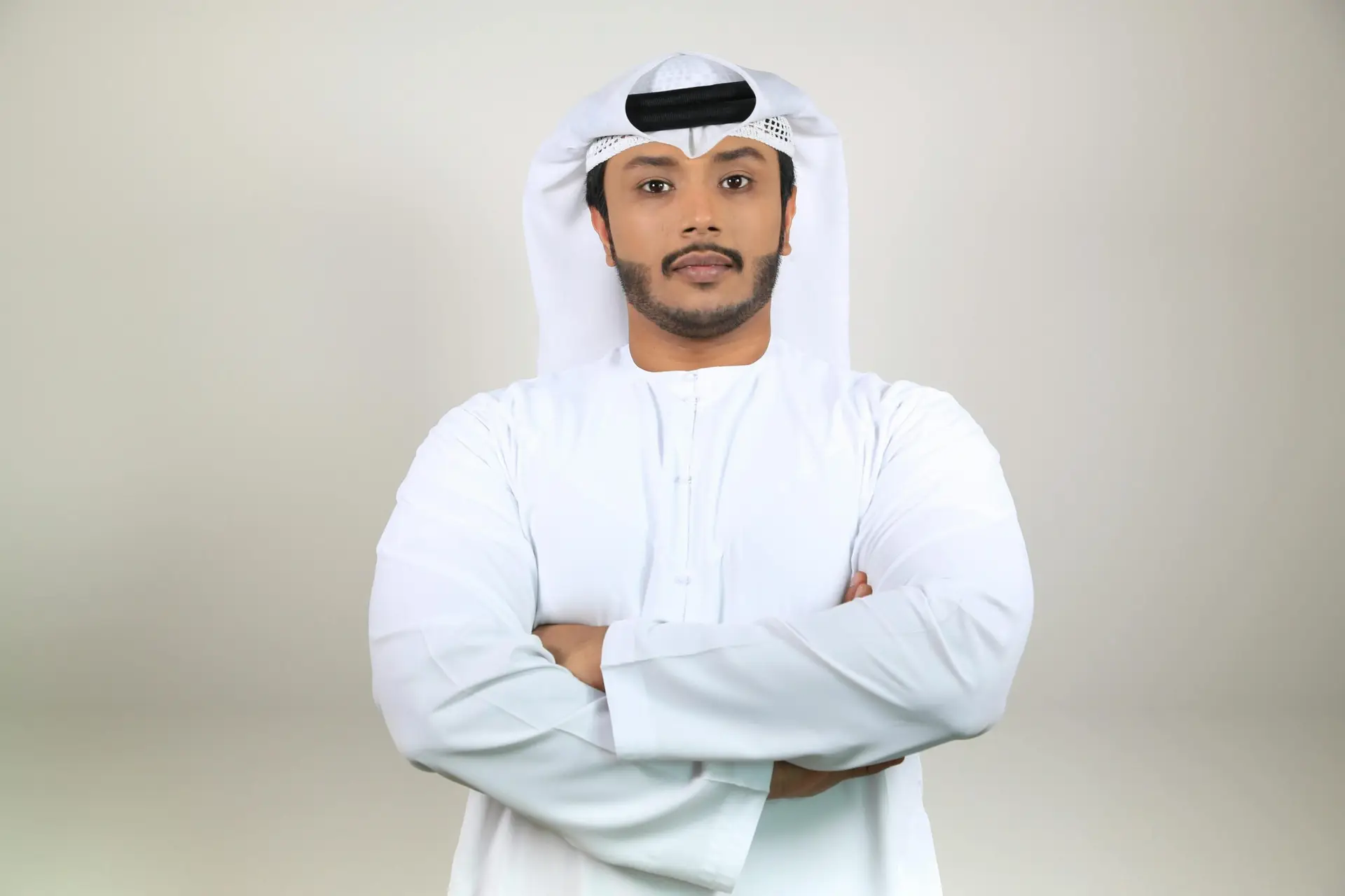 Young Middle Eastern man in white thobe standing confidently indoors.